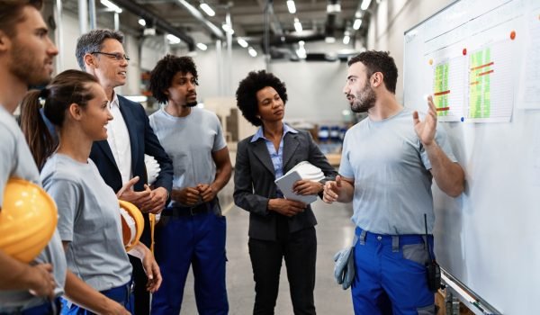 Young manual worker presenting new business strategy to company managers and his colleagues in a factory.